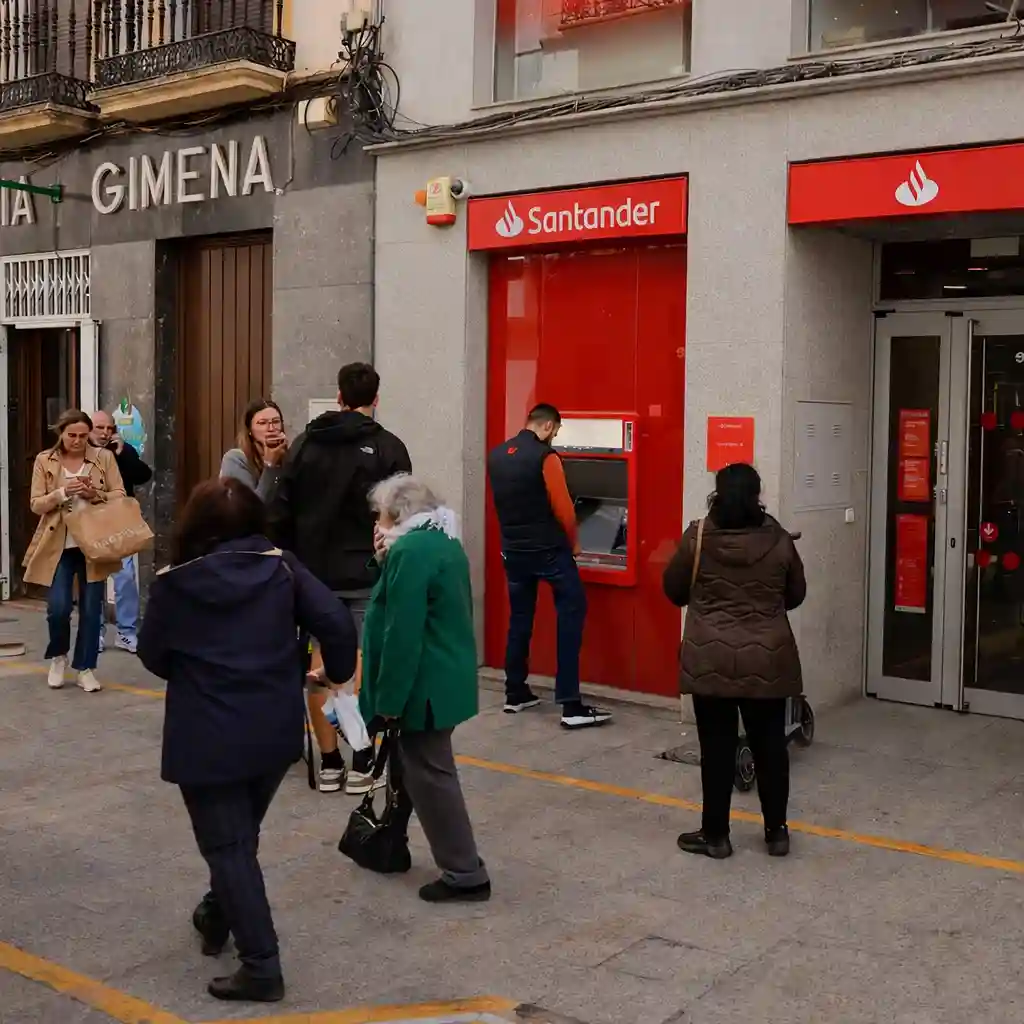 Santander bank branch with customers using the ATM outside and people walking by in front of the store.