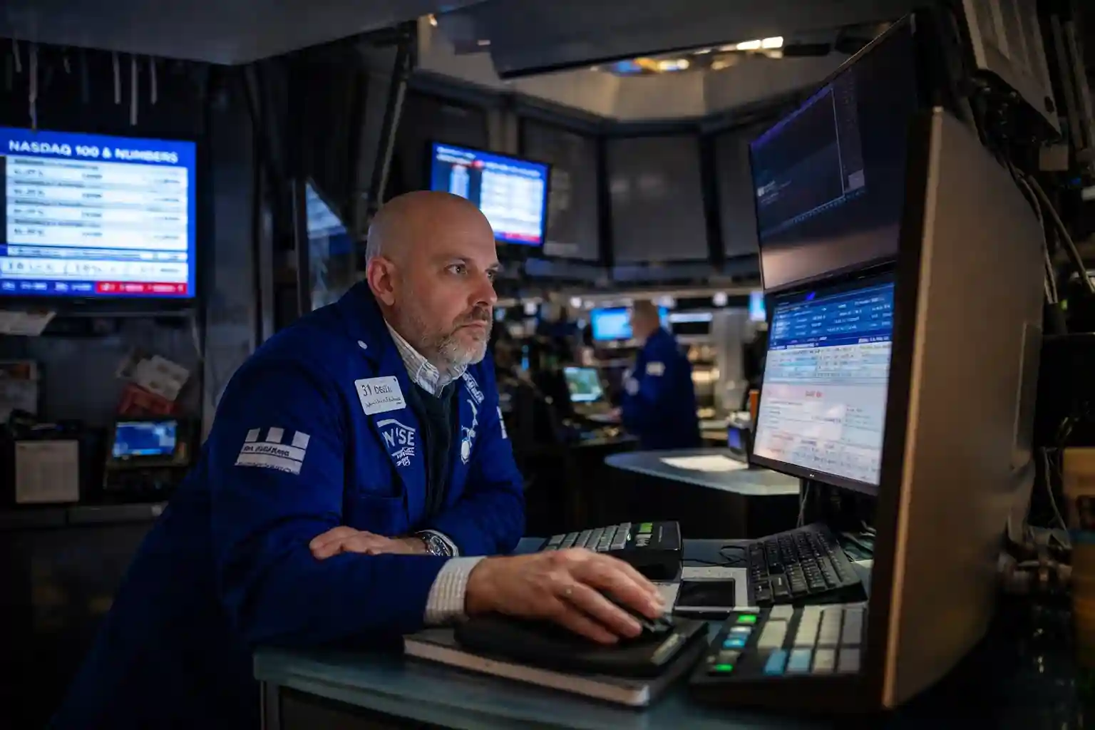 Stock trader working at his desk with multiple screens showing market data